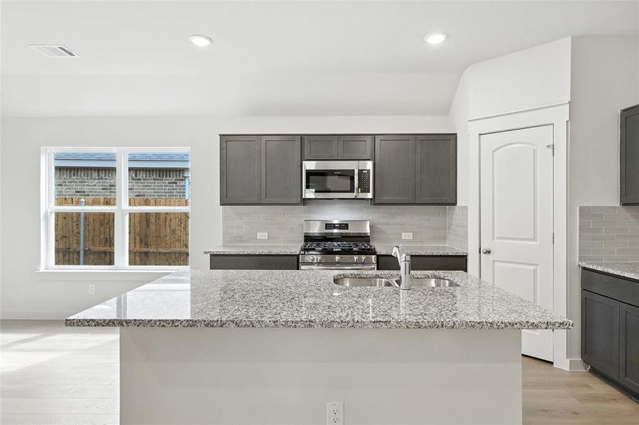 Kitchen featuring stainless steel appliances, light stone counters, light wood-style flooring, backsplash, and a center island with sink