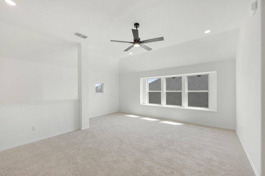 Empty bedroom with vaulted ceiling, ceiling fan, carpet flooring, and large windows with natural light