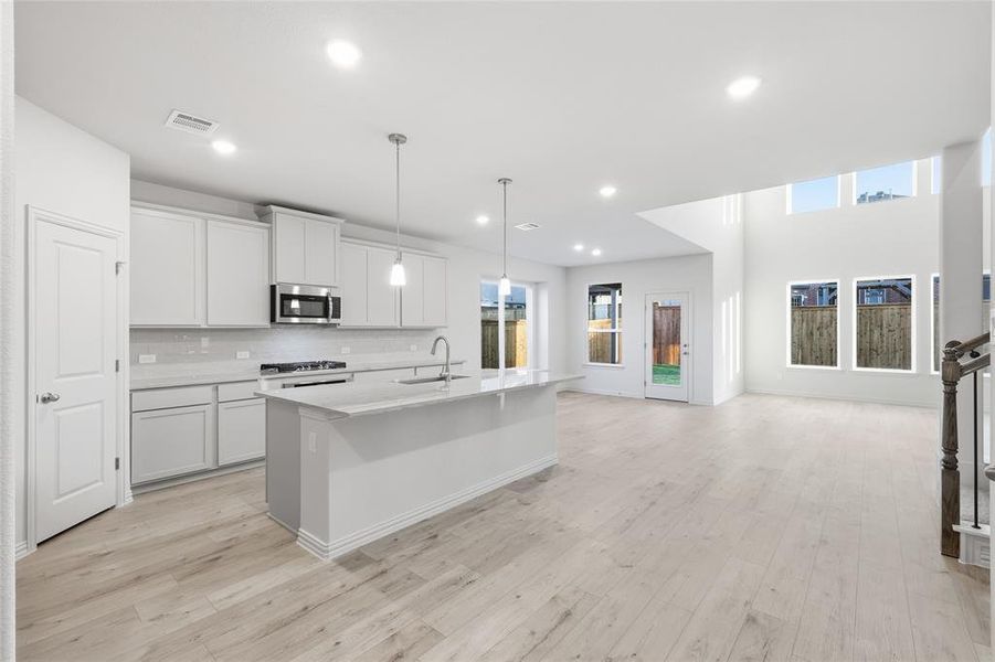 Kitchen with decorative light fixtures, a kitchen island with sink, open floor plan, appliances with stainless steel finishes, and light wood finished floors
