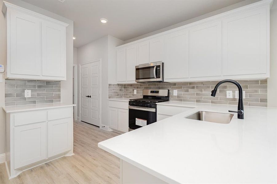 Kitchen with appliances with stainless steel finishes, tasteful backsplash, light wood finished floors, recessed lighting, and light countertops