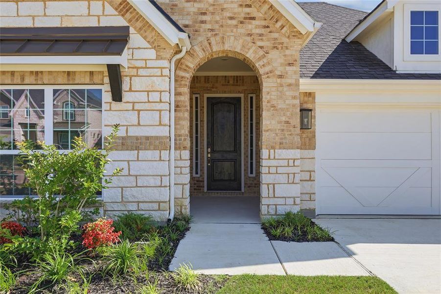 Entryway featuring a dark wood door, arched brick accents, stone and brick facade, a covered front porch, and a concrete driveway