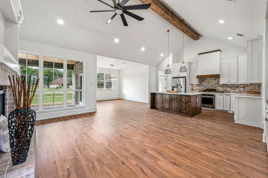 Kitchen with pendant lighting, an island with sink, beam ceiling, appliances with stainless steel finishes, and light hardwood / wood-style flooring