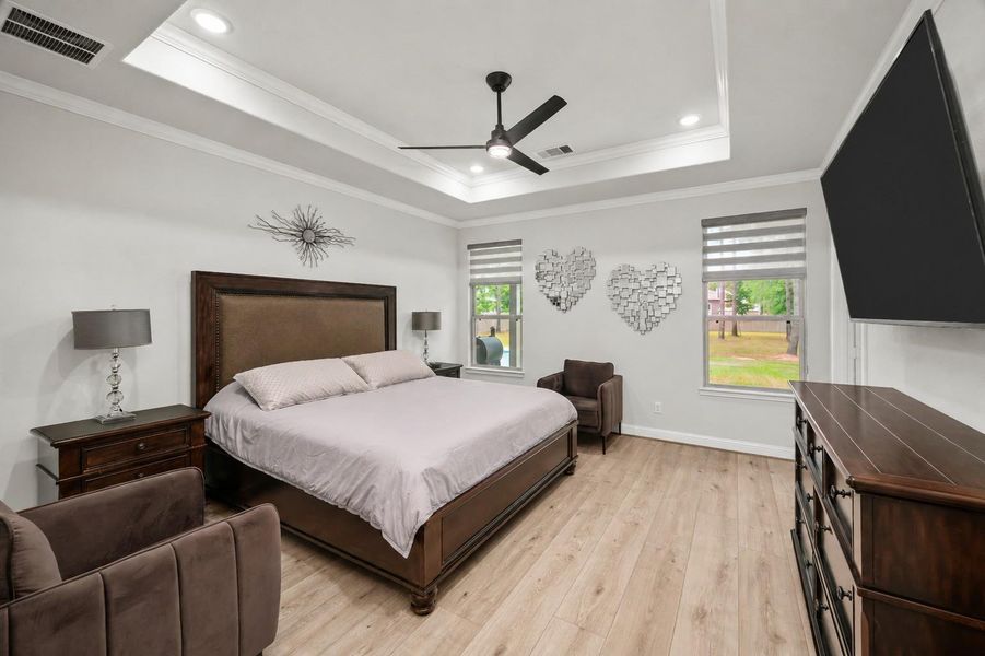 The primary bedroom suite with tray ceiling, crown molding, modern ceiling fan, and views of the backyard.