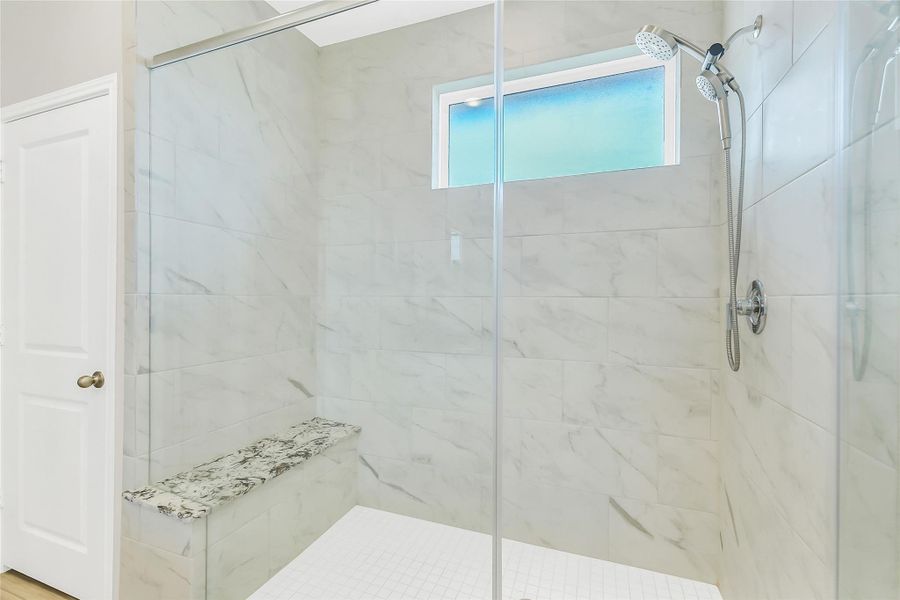 A glass-enclosed walk-in shower features elegant tile surround and a built-in bench, offering a luxurious, high-end experience.