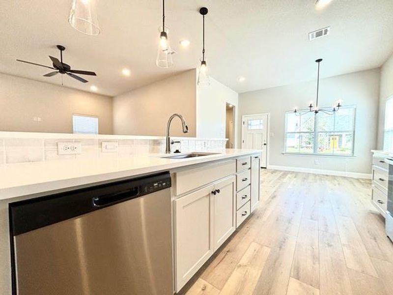 Kitchen featuring stainless steel dishwasher, ceiling fan with notable chandelier, sink, pendant lighting, and white cabinets