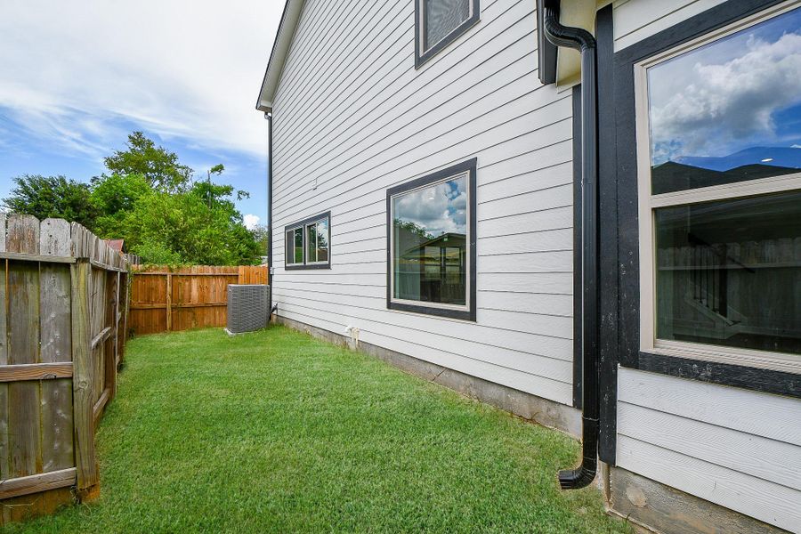 This is a well-maintained side yard with a lush green lawn, bordered by a wooden fence for privacy. The exterior of the home features clean, modern siding with multiple windows providing natural light inside. An air conditioning unit is present, indicating central air. It's a tidy outdoor space with potential for personal landscaping or a patio setup. This is a well-maintained side yard with a lush green lawn, bordered by a wooden fence for privacy. The exterior of the home features clean, modern siding with multiple windows providing natural light inside. An air conditioning unit is present, indicating central air. It's a tidy outdoor space with potential for personal landscaping or a patio setup.