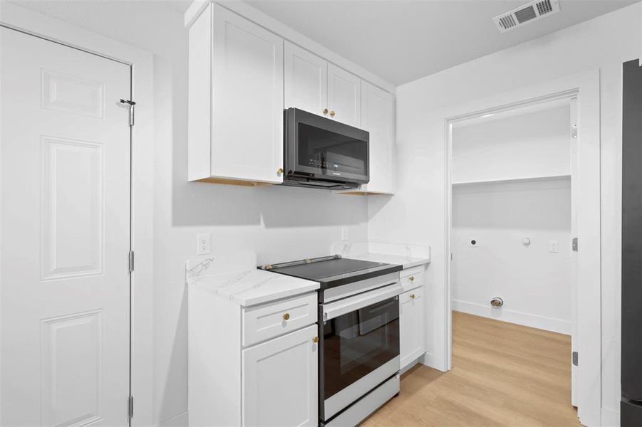 Kitchen with stainless steel range with electric cooktop, white cabinetry, light hardwood / wood-style flooring, and light stone countertops