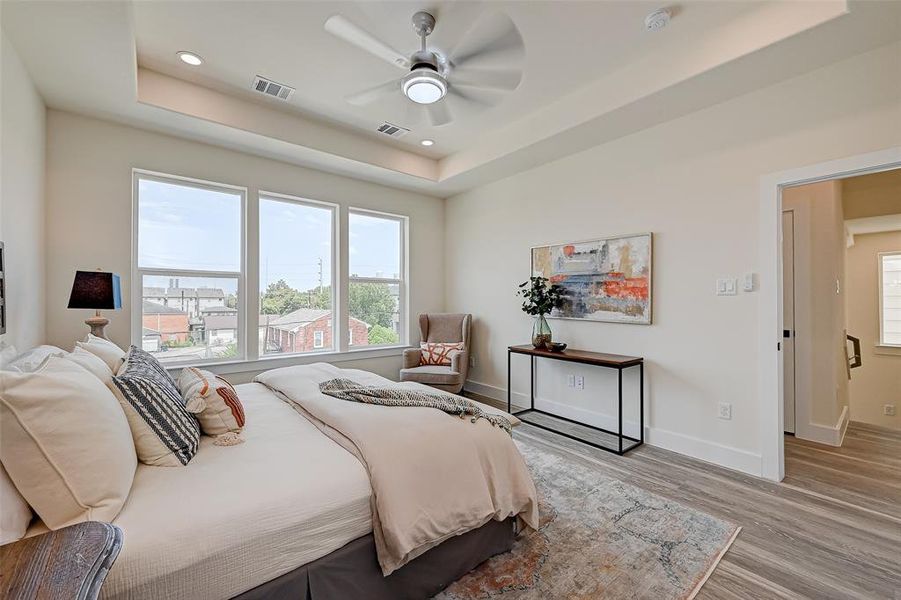 Bright and spacious bedroom with large windows offering natural light. Features a modern ceiling fan, wood flooring, and tasteful decor. Ideal for comfort and relaxation.