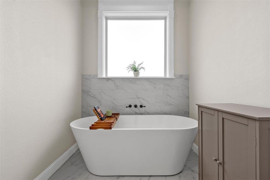Primary bath featuring a freestanding soaking tub beneath a privacy window. Primary bath featuring a freestanding soaking tub beneath a privacy window.