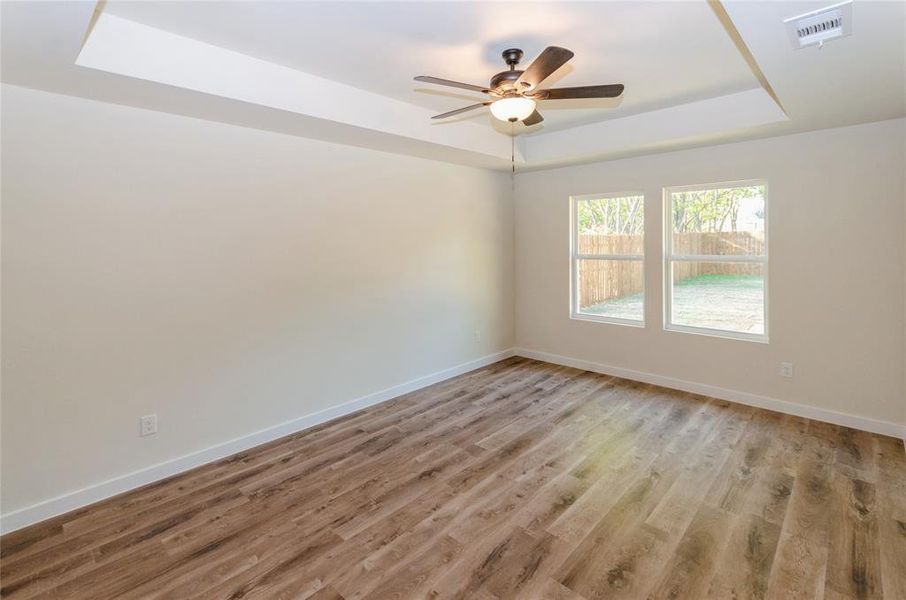 Unfurnished room featuring light hardwood / wood-style flooring, a tray ceiling, and ceiling fan