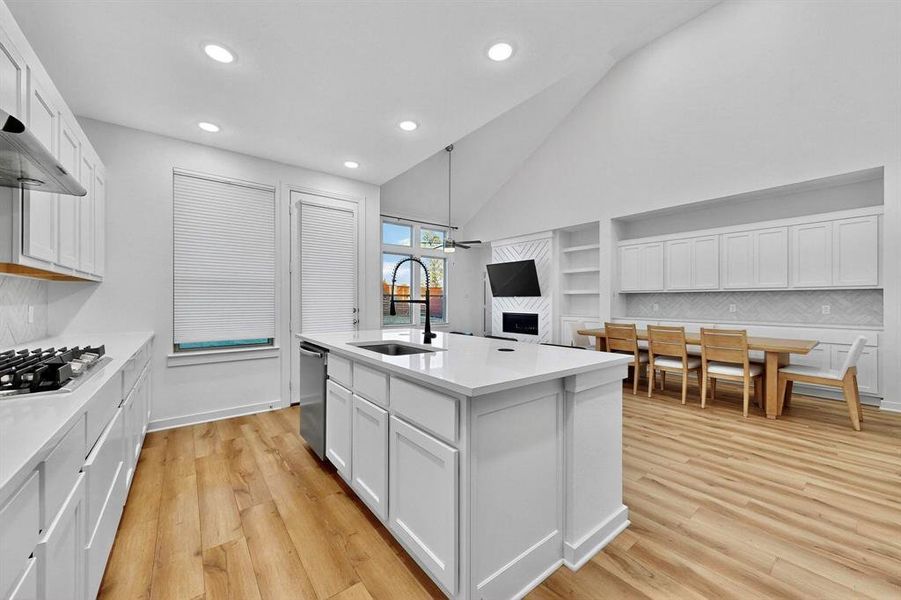 Kitchen featuring white cabinetry, backsplash, light wood finished floors, open floor plan, and high vaulted ceiling Kitchen featuring white cabinetry, backsplash, light wood finished floors, open floor plan, and high vaulted ceiling