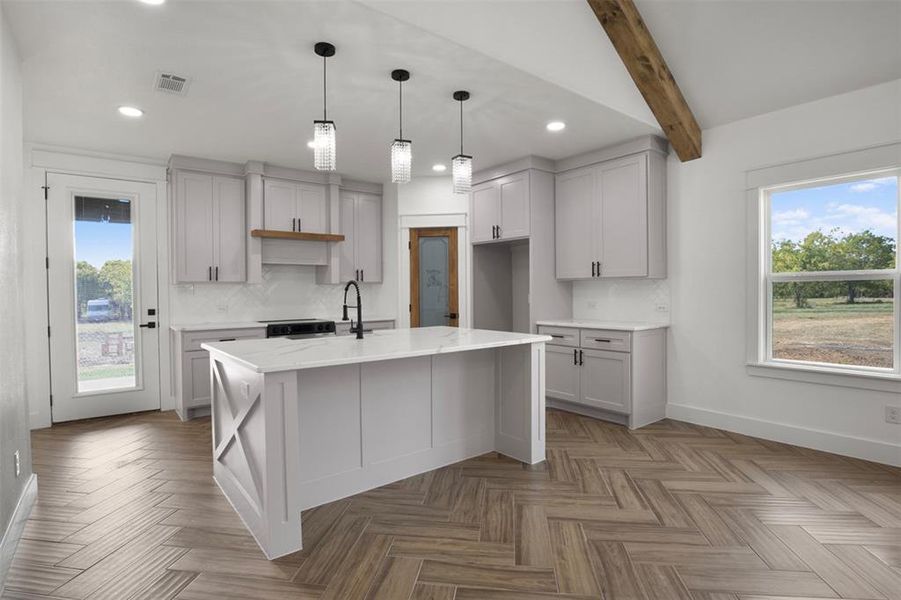 Kitchen with light stone counters, beamed ceiling, decorative backsplash, and a kitchen island with sink