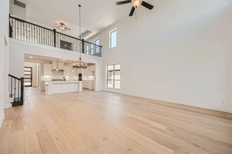 Unfurnished living room with ceiling fan with notable chandelier, a high ceiling, light hardwood / wood-style floors, and sink