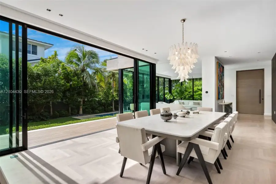 Floor-to-ceiling sliding glass walls, light-toned chevron-patterned wood-finish flooring, sculptural multi-tier chandelier, and recessed ceiling lighting