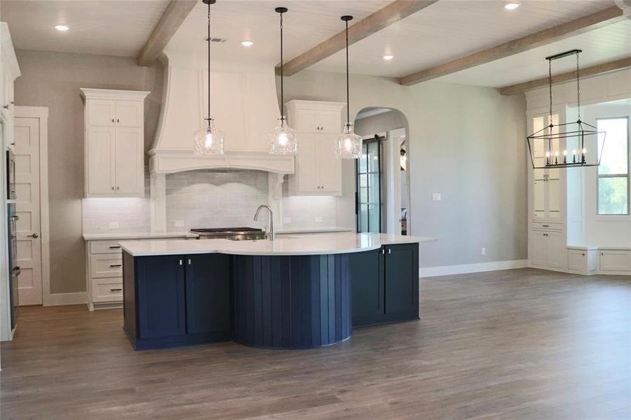 Kitchen with arched walkways, light countertops, baseboards, beamed ceiling, and decorative backsplash