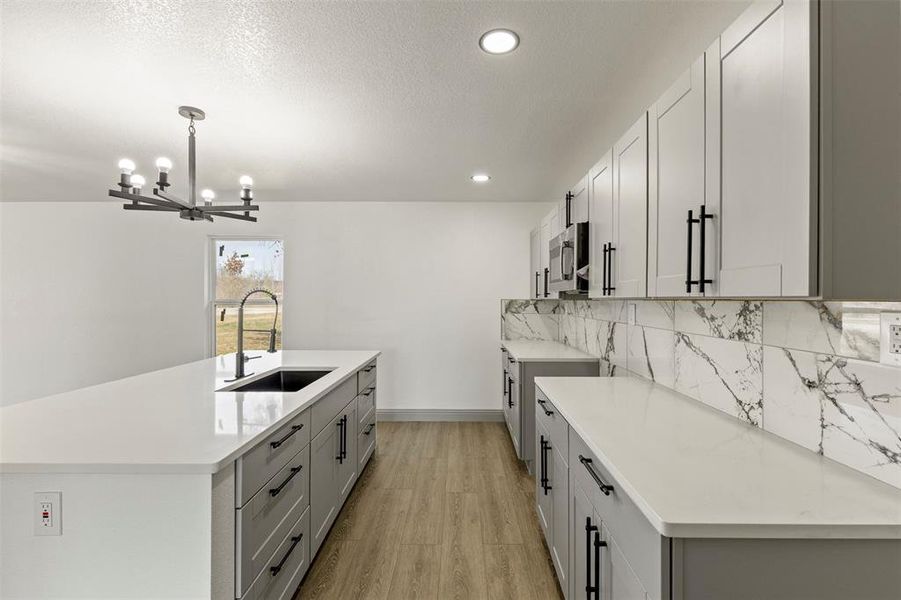 Kitchen featuring light wood-style floors, an island with sink, light stone countertops, gray cabinets, and a textured ceiling
