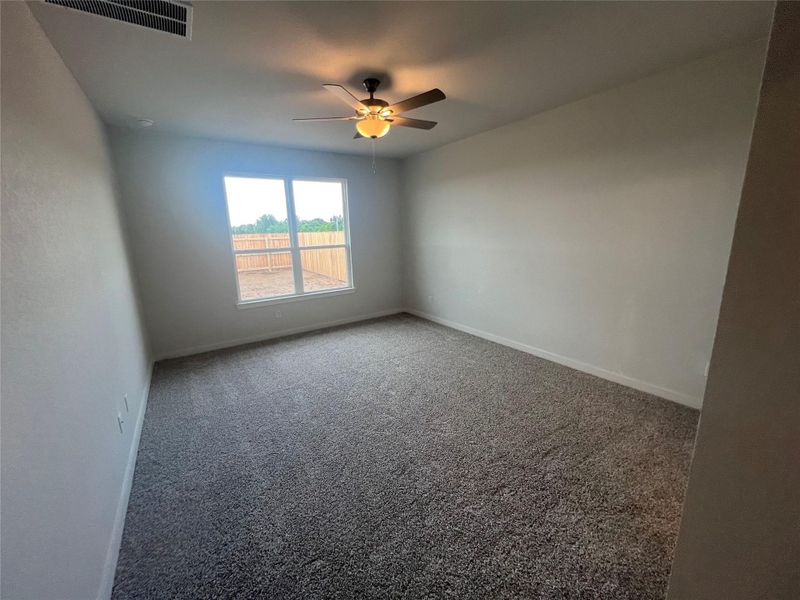 A well-lit bedroom featuring a functional ceiling fan and a soft, inviting carpet.