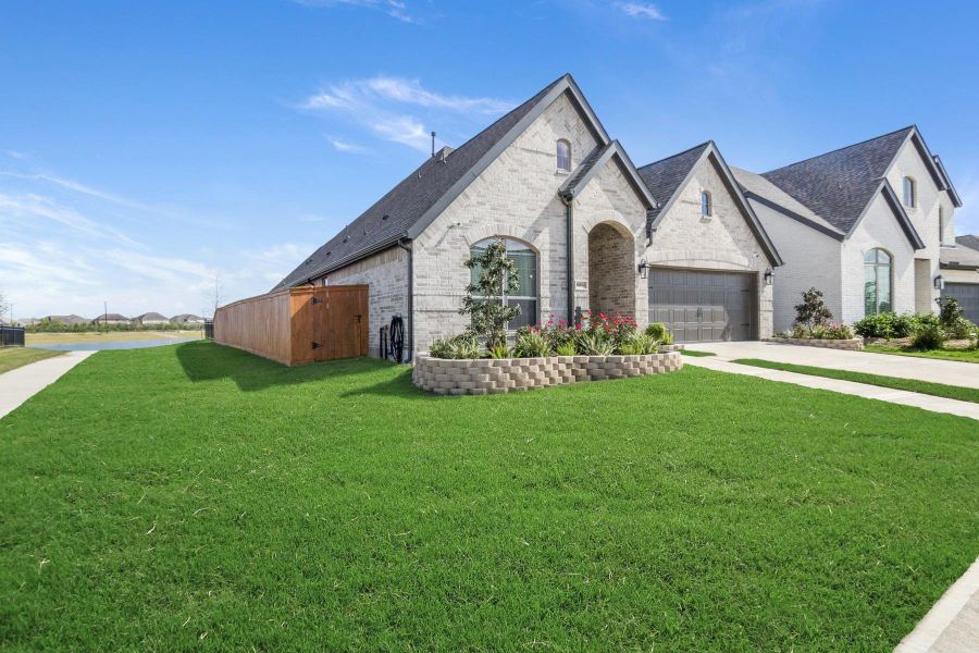 This photo showcases a modern, single-story brick home with a well-maintained lawn and a landscaped front yard. It features a two-car garage, arched entryway, and a spacious driveway, situated in a suburban setting with a clear blue sky overhead.