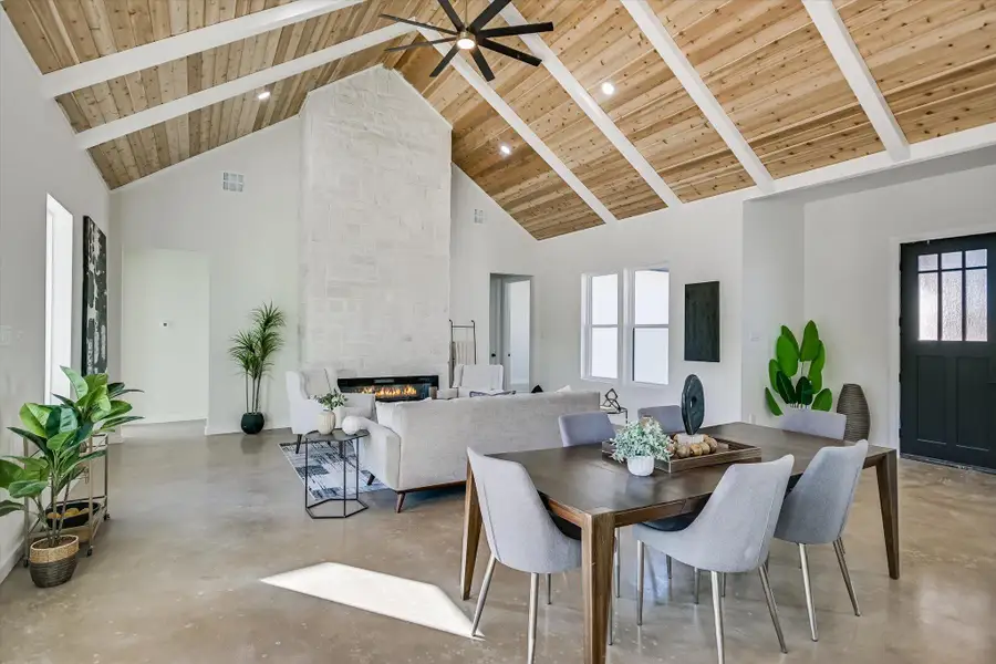 Dining space featuring concrete floors, high vaulted ceiling, a fireplace, a wood ceiling with exposed beams, and a ceiling fan