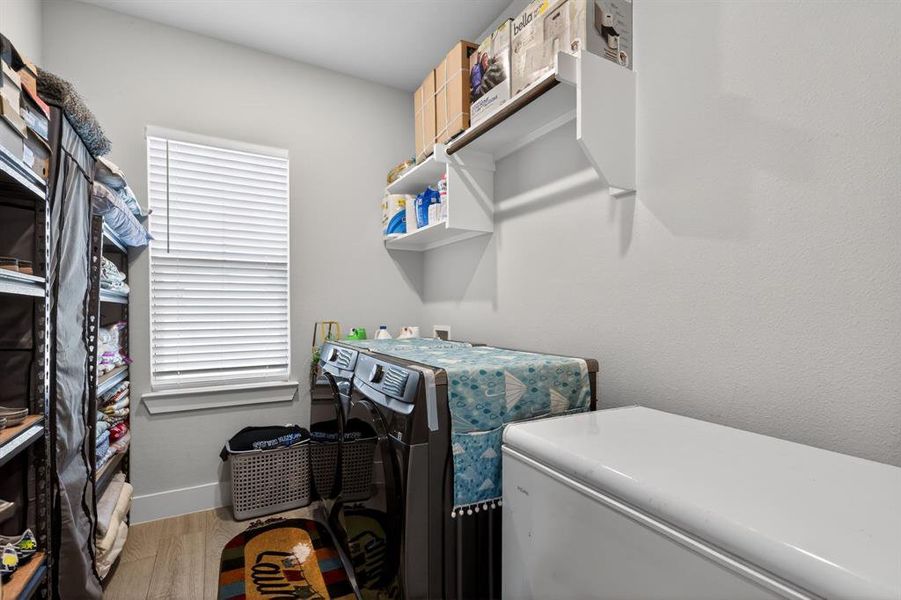 Well-appointed utility area featuring a window with blinds, overhead shelving, and light-toned flooring