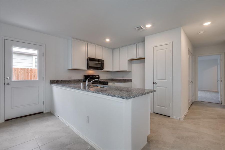 Kitchen with black appliances, white cabinets, kitchen peninsula, and light tile floors Kitchen with black appliances, white cabinets, kitchen peninsula, and light tile floors