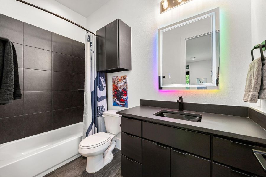 Modern Secondary bathroom featuring a sleek black vanity with ample storage, a stylish backlit mirror, and a shower-tub combo with dark tile accents. Modern Secondary bathroom featuring a sleek black vanity with ample storage, a stylish backlit mirror, and a shower-tub combo with dark tile accents.