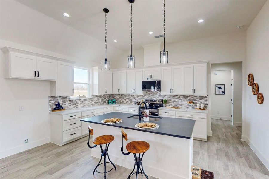 Kitchen featuring light wood-type flooring, stainless steel appliances, sink, a center island with sink, and white cabinetry