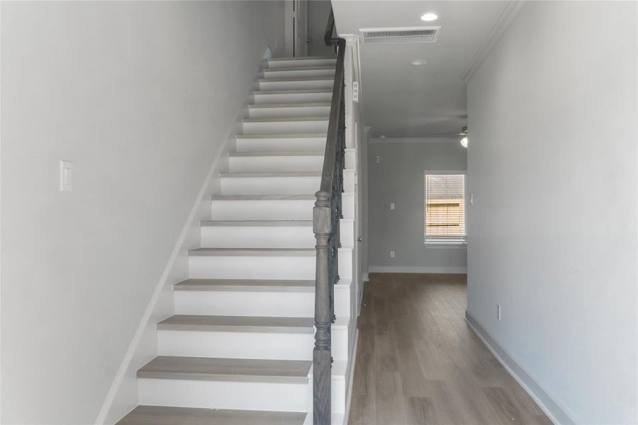 This photo shows a bright, modern hallway with light wood flooring and a staircase with a dark handrail. There's a window at the end, providing natural light.