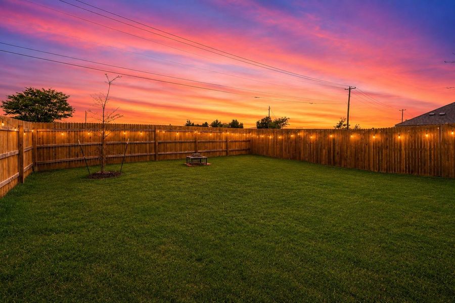 Expansive backyard featuring a lush green lawn, full privacy fencing, string lighting, a small tree, and a fire pit Expansive backyard featuring a lush green lawn, full privacy fencing, string lighting, a small tree, and a fire pit
