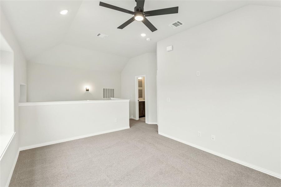 Empty bedroom with vaulted ceiling, ceiling fan, carpet flooring, and doorway to ensuite bathroom Empty bedroom with vaulted ceiling, ceiling fan, carpet flooring, and doorway to ensuite bathroom