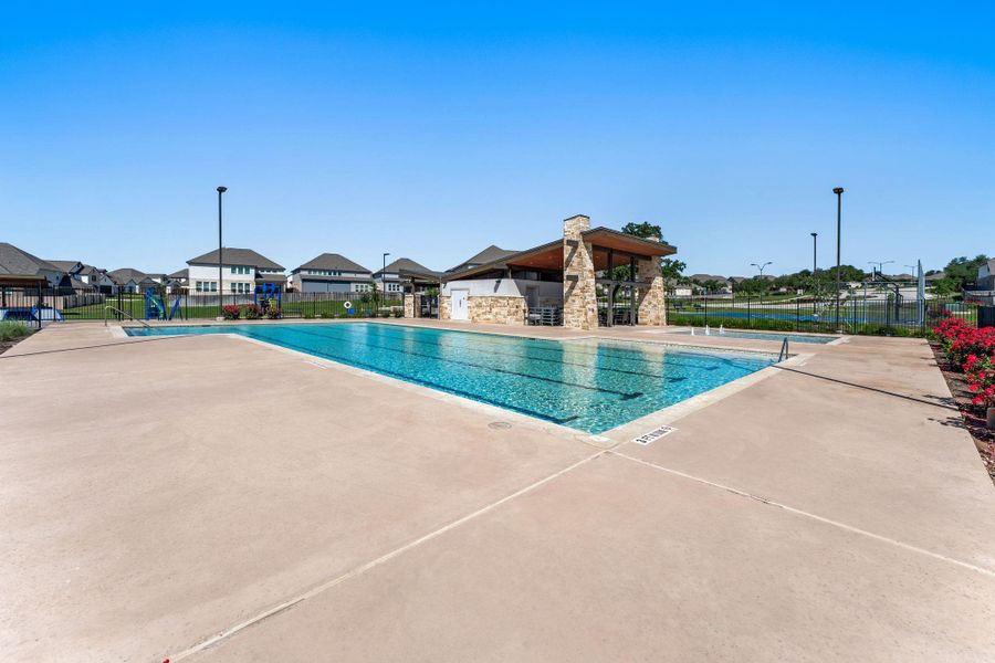 Community swimming pool with a concrete deck, an adjacent splash pad, and a stone-clad pavilion