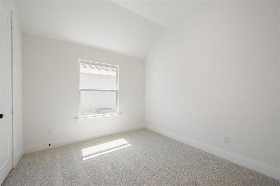 Carpeted empty room featuring vaulted ceiling and baseboards Carpeted empty room featuring vaulted ceiling and baseboards