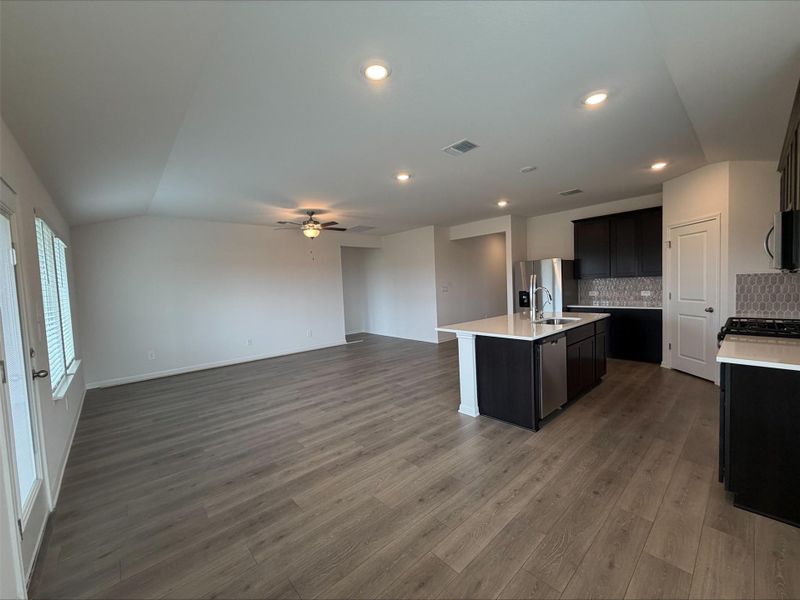 Kitchen featuring tasteful backsplash, a kitchen island with sink, dark wood-style flooring, open floor plan, and lofted ceiling