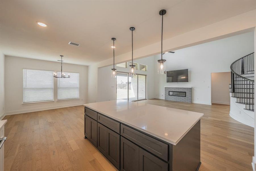 Open concept living space featuring light hardwood flooring, a kitchen island with a white countertop and dark cabinetry, and pendant lighting