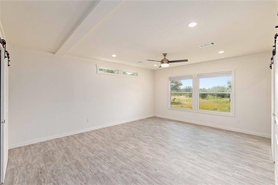 Spacious room featuring wood-finish flooring, white walls, and a ceiling fan