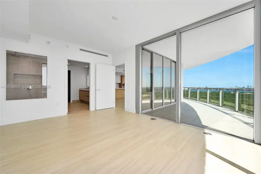 Interior space featuring wood-finish flooring, floor-to-ceiling sliding glass doors, a wrap-around balcony with a metal railing, and a glass-enclosed shower with tiled wall surrounds