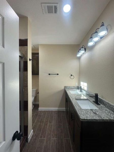 Full bathroom with double vanity, wood tiled floors, and a stall shower
