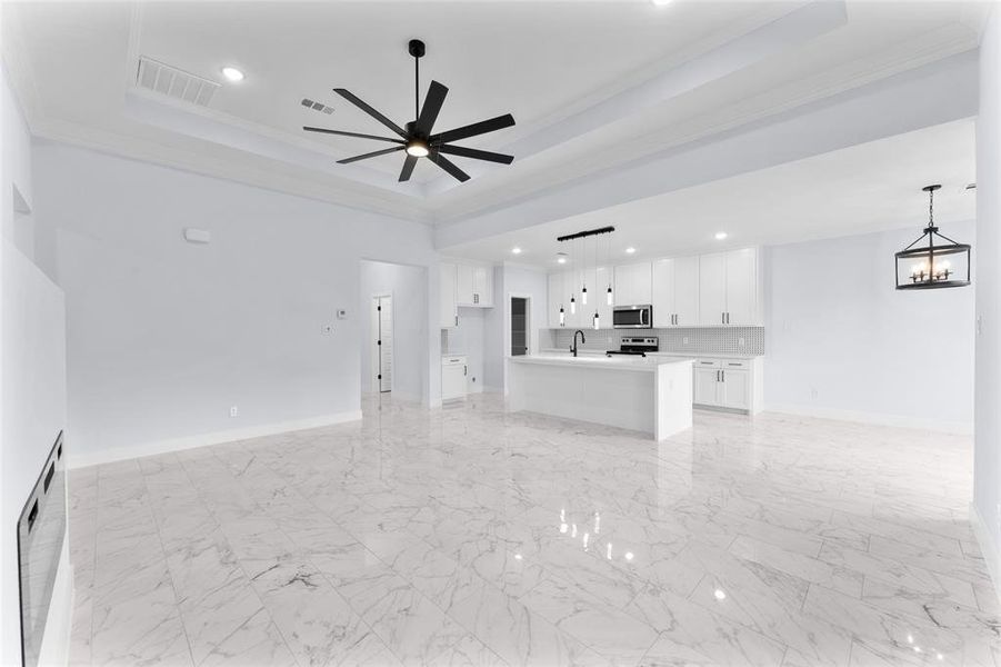 Unfurnished living room featuring ceiling fan with notable chandelier, a raised ceiling, ornamental molding, and sink