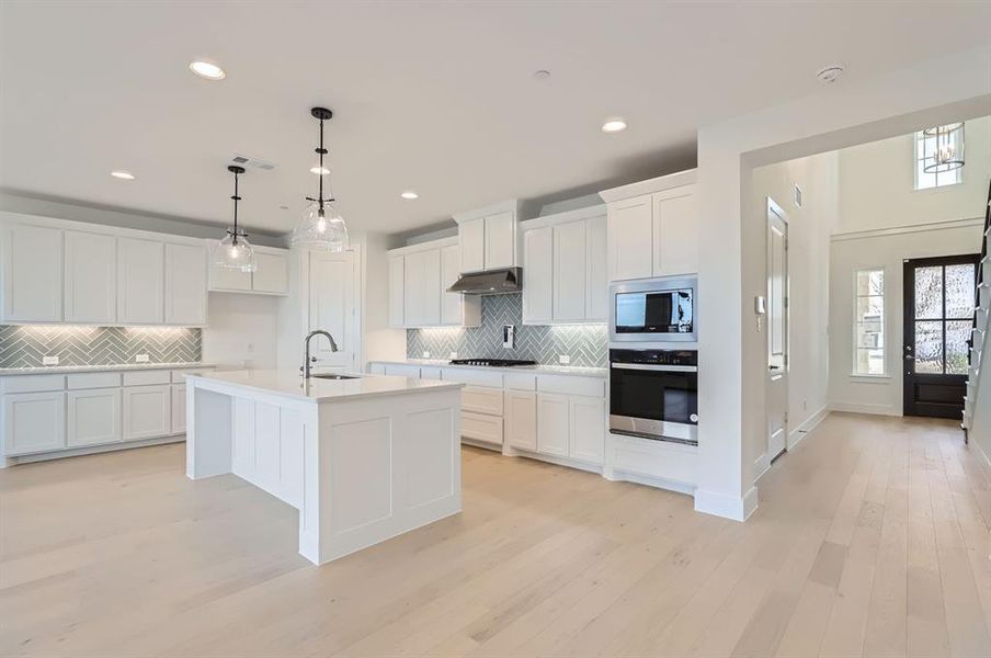 Kitchen with a center island with sink, sink, tasteful backsplash, white cabinetry, and stainless steel appliances