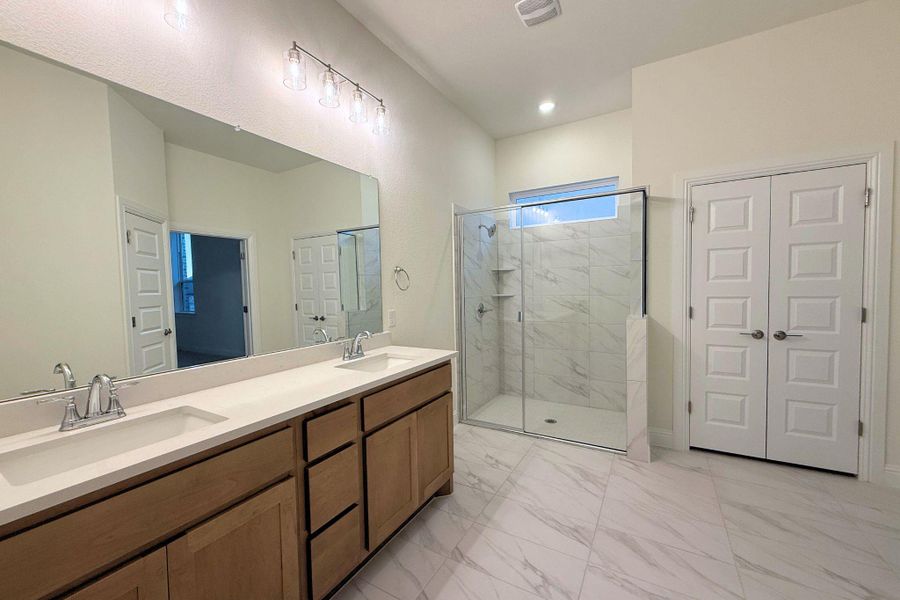 Full bathroom featuring light marble finish flooring, double vanity, a marble finish shower, and a closet