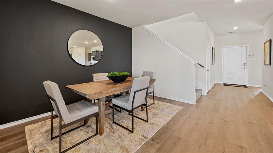Dining area featuring a dark accent wall, a round mirror, and wood flooring Dining area featuring a dark accent wall, a round mirror, and wood flooring