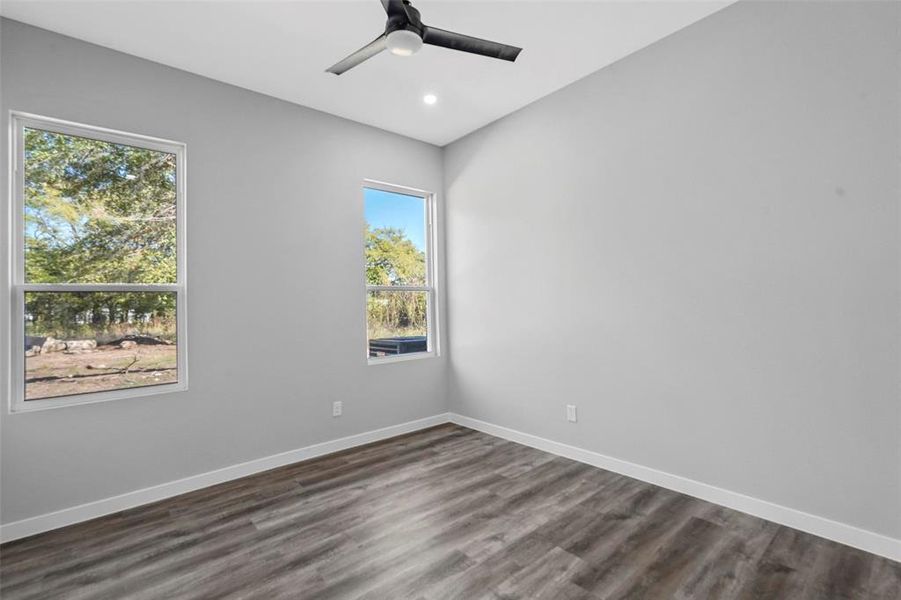 Spare room featuring dark wood-type flooring, a wealth of natural light, and ceiling fan