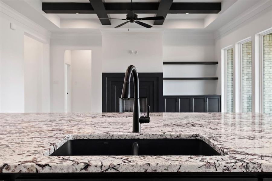 Room details with ceiling fan, coffered ceiling, light stone counters, sink, and beamed ceiling