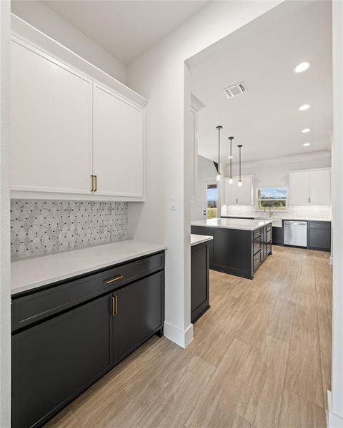 Kitchen featuring tasteful backsplash, two tone cabinets, pendant lighting, dishwasher, and light wood-type flooring