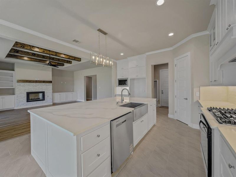 Kitchen with white cabinets, light stone counters, appliances with stainless steel finishes, crown molding, and a stone fireplace Kitchen with white cabinets, light stone counters, appliances with stainless steel finishes, crown molding, and a stone fireplace