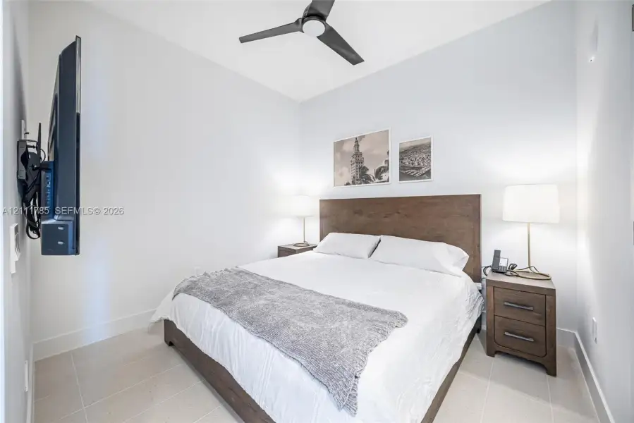 Neutral-toned tile flooring, matte black ceiling fan, and wall-mounted television bracket