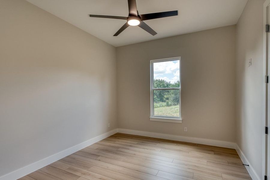 An airy bedroom with hardwood-style flooring and a contemporary ceiling fan offers peaceful views.