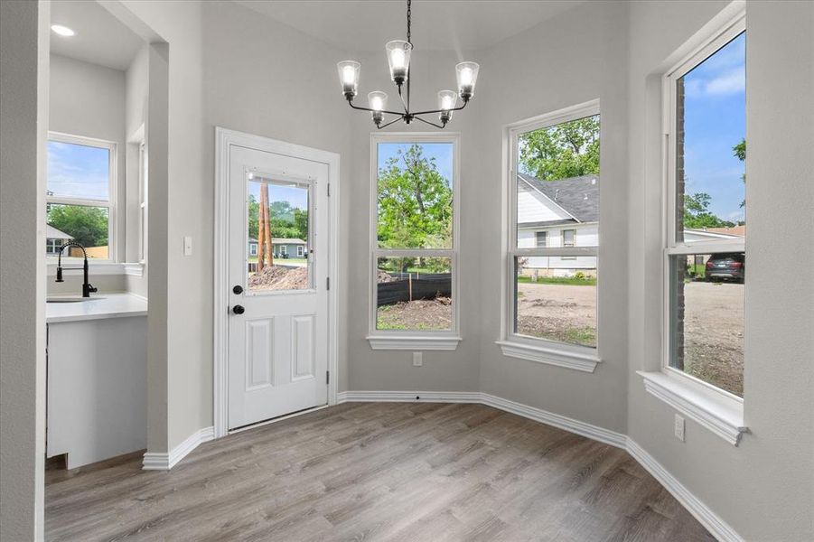 Bay window dining nook featuring a contemporary chandelier, light wood-finish flooring, and a glass-paneled exterior door