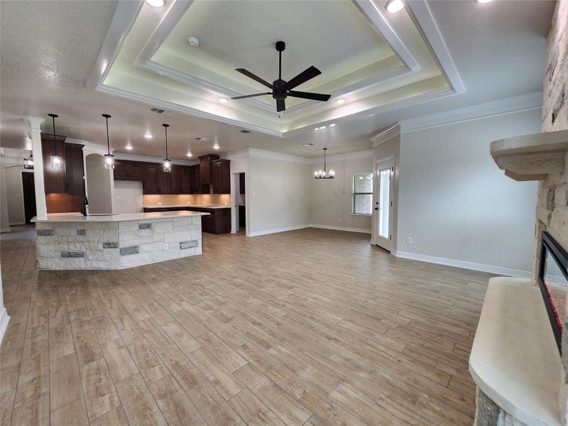 A striking open floorplan with a stone-clad kitchen island and a tiered ceiling featuring recessed lighting. A striking open floorplan with a stone-clad kitchen island and a tiered ceiling featuring recessed lighting.