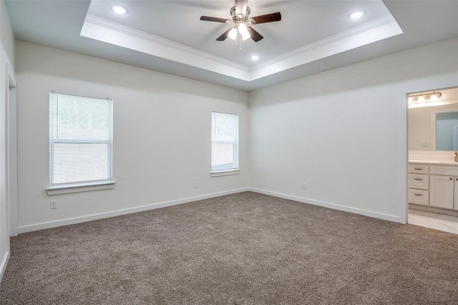 Unfurnished bedroom featuring multiple windows, ensuite bath, and a tray ceiling